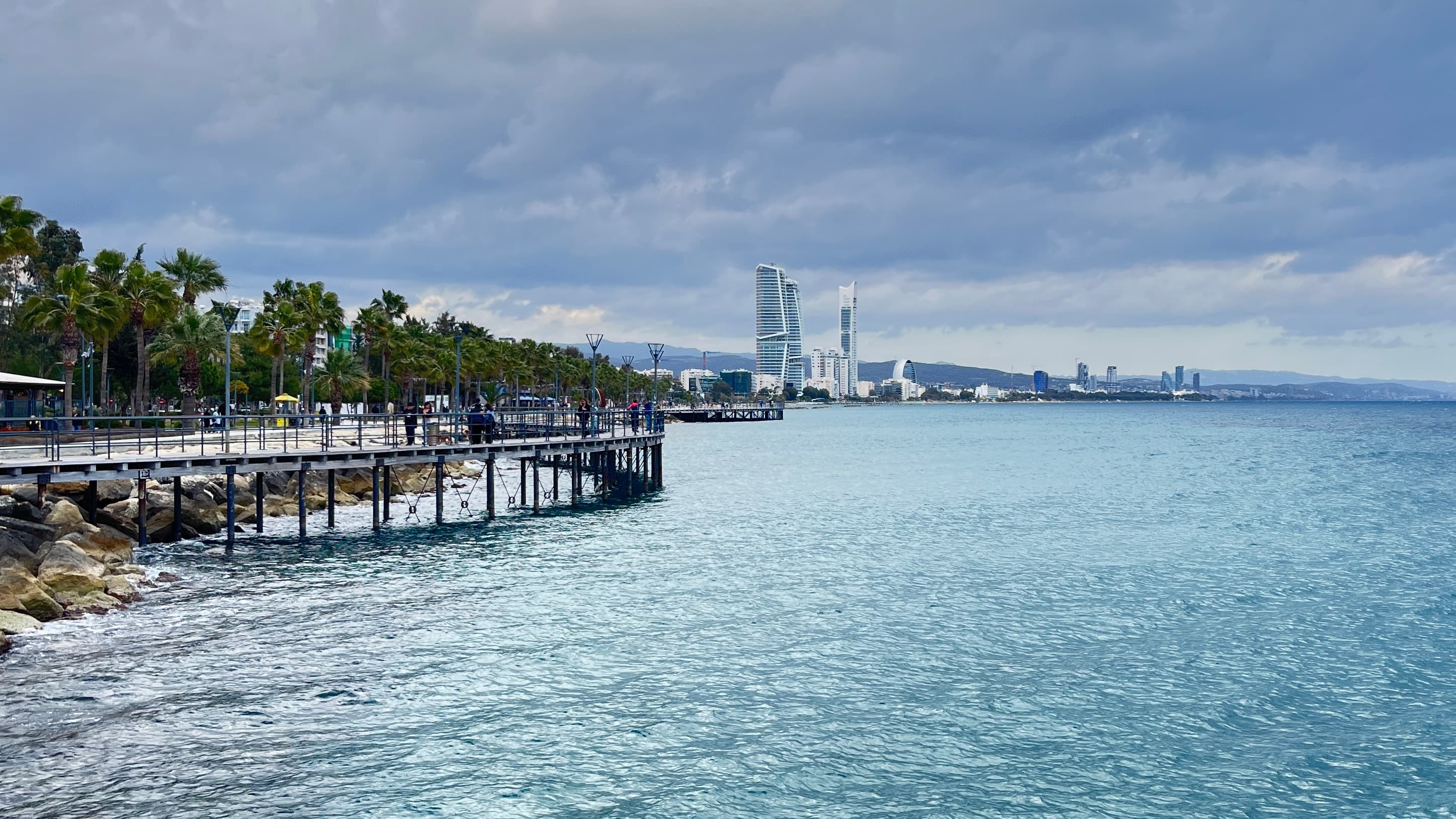 The pier at the Molos seafront park in Limassol, the waterfront towers behind it across the bay